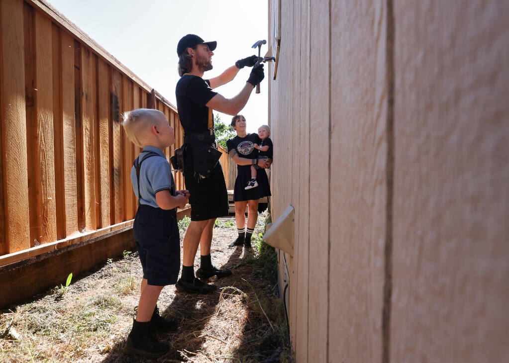 Trevor Meusx pulls a window frame with dry rot while his wife, Audra, and sons, Brixton, 4, and Cillian, 1, watch at the home they are renting from Audra's brother in Santa Rosa on Wednesday, June 9, 2021.  (Christopher Chung/ The Press Democrat)