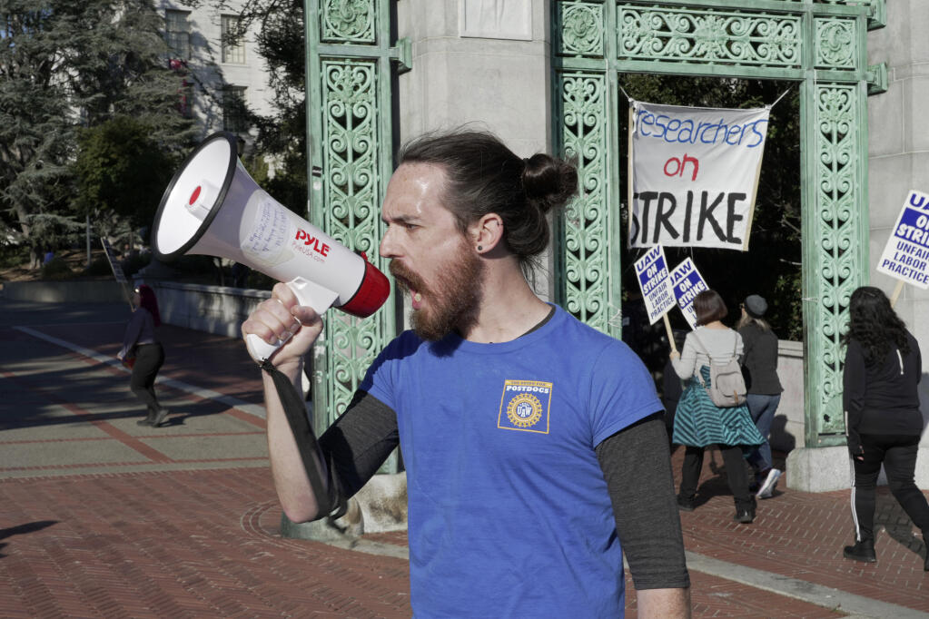 Tyler Manning, a post-doctoral researcher at UC Berkeley, leads a chant as striking academic workers picket on the University of California, Berkeley campus in Berkeley, Calif., Wednesday, Dec. 7, 2022. A month into the nation's largest strike involving higher education, classes are being cancelled and important research is being disrupted at the 10 campuses of the University of California. (AP Photo/Terry Chea)