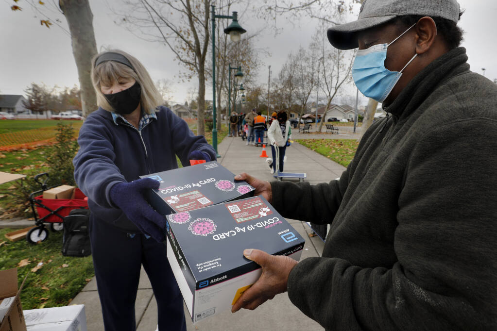 Volunteer Linda Hoile hands two boxes of rapid COVID-19 tests to Juma Nalik during a food distribution by the Redwood Empire Food Bank at Martin Luther King Jr. Memorial Park in Santa Rosa on Monday, Dec. 20, 2021. (Beth Schlanker/The Press Democrat)