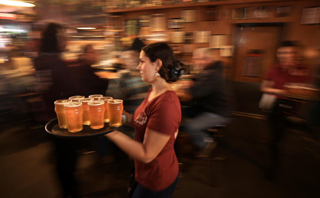 Russian River Brewing Co. server Erika Corella of Rohnert Park, takes a tray of Pliny the Younger to a table, Friday, March 25, 2022, at the brewpub in Santa Rosa. (Kent Porter/The Press Democrat file)