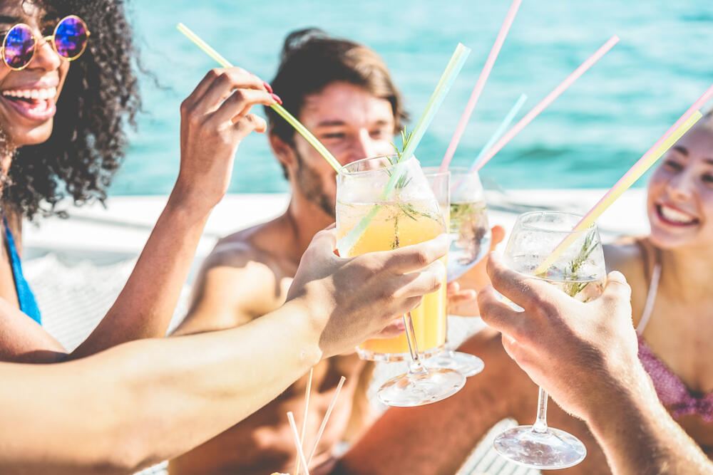 Five young adults toast tropical cocktails at a beach. (DisobeyArt / Shutterstock)
