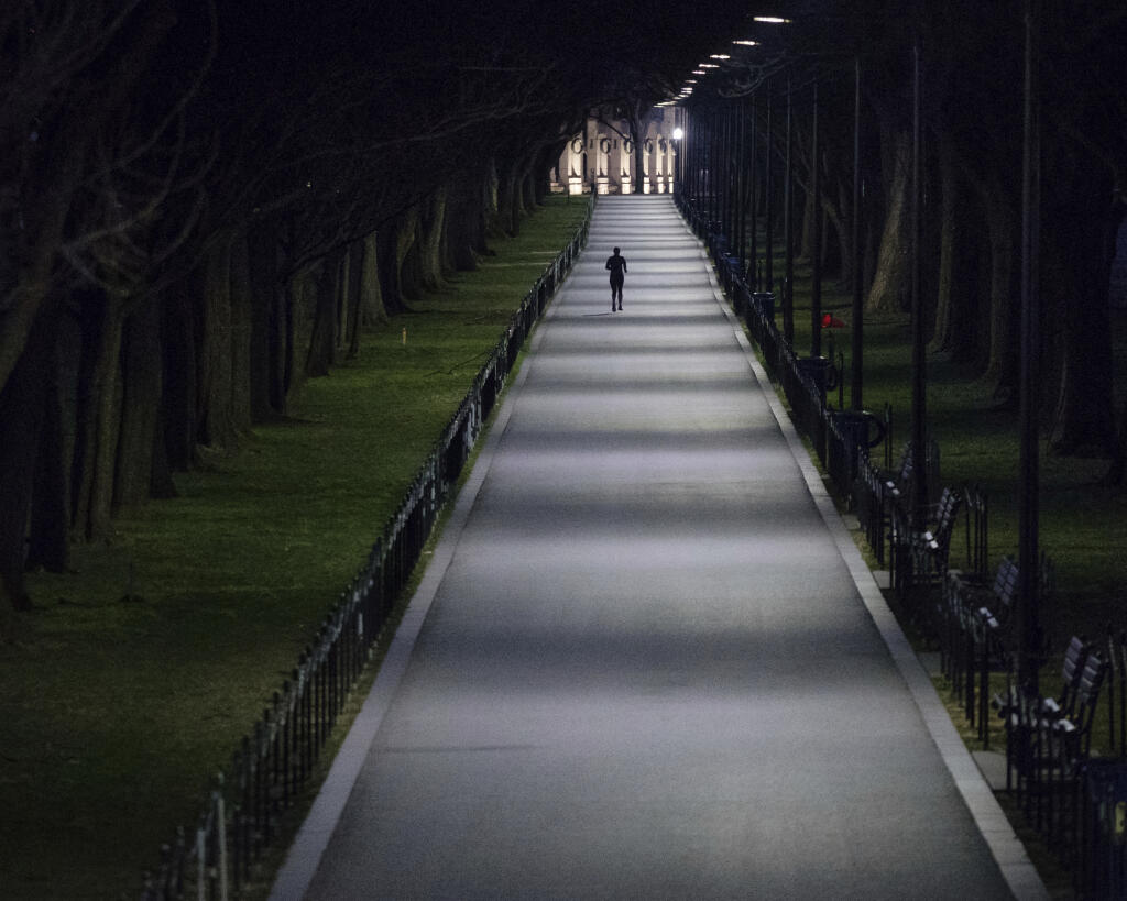 An solitary runner is silhouetted against the tree lined path along the National Mall before daybreak, Thursday, March 15, 2018. (AP Photo/J. David Ake)