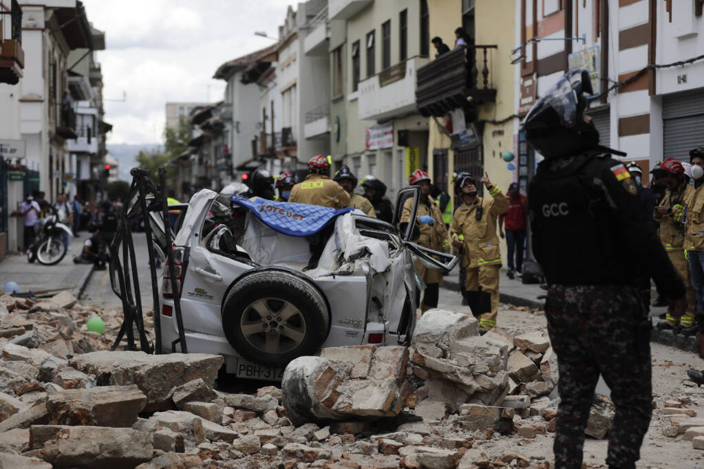 A police officer looks up next to a car crushed by debris after an earthquake shook Cuenca, Ecuador, Saturday, March 18, 2023. The U.S. Geological Survey reported an earthquake with a magnitude of 6.7 on Saturday about 50 miles south of Guayaquil .(AP Photo/Xavier Caivinagua)