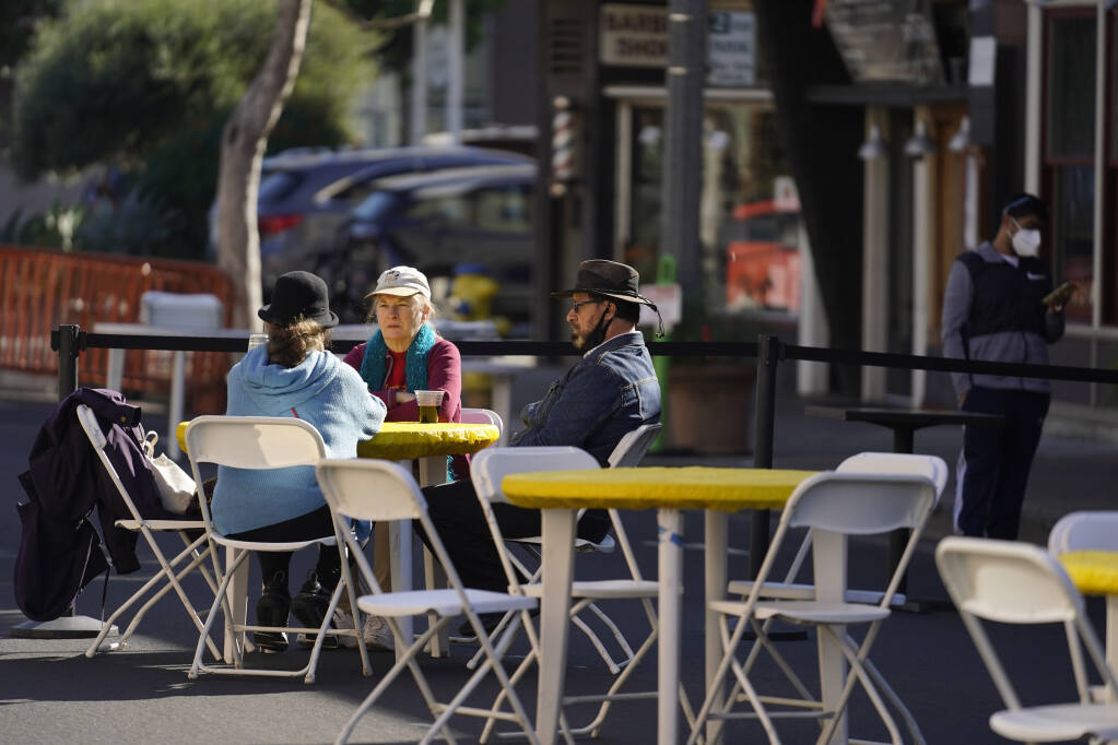 People sit at tables on a street closed off for outdoor dining Friday, Dec. 4, 2020, in Sausalito, Calif. The health officers in six San Francisco Bay Area regions have issued a new stay-at-home order as the number of virus cases surge and hospitals fill. The changes announced Friday will take effect in most of the area at 10 p.m. Sunday and last through Jan. 4. It means restaurants will have to close to indoor and outdoor dining, bars and wineries must close along with hair and nail salons and playgrounds. (AP Photo/Eric Risberg)