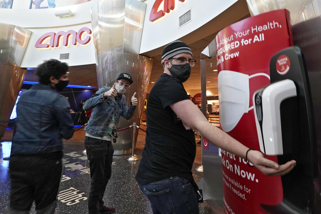 Alston Huff, right, uses hand sanitizer before seeing a movie with his friends Anes Hasi, left, and Jamin Scotti at the AMC 16 theater, Monday, March 15, 2021, in Burbank, Calif. (AP Photo/Mark J. Terrill)