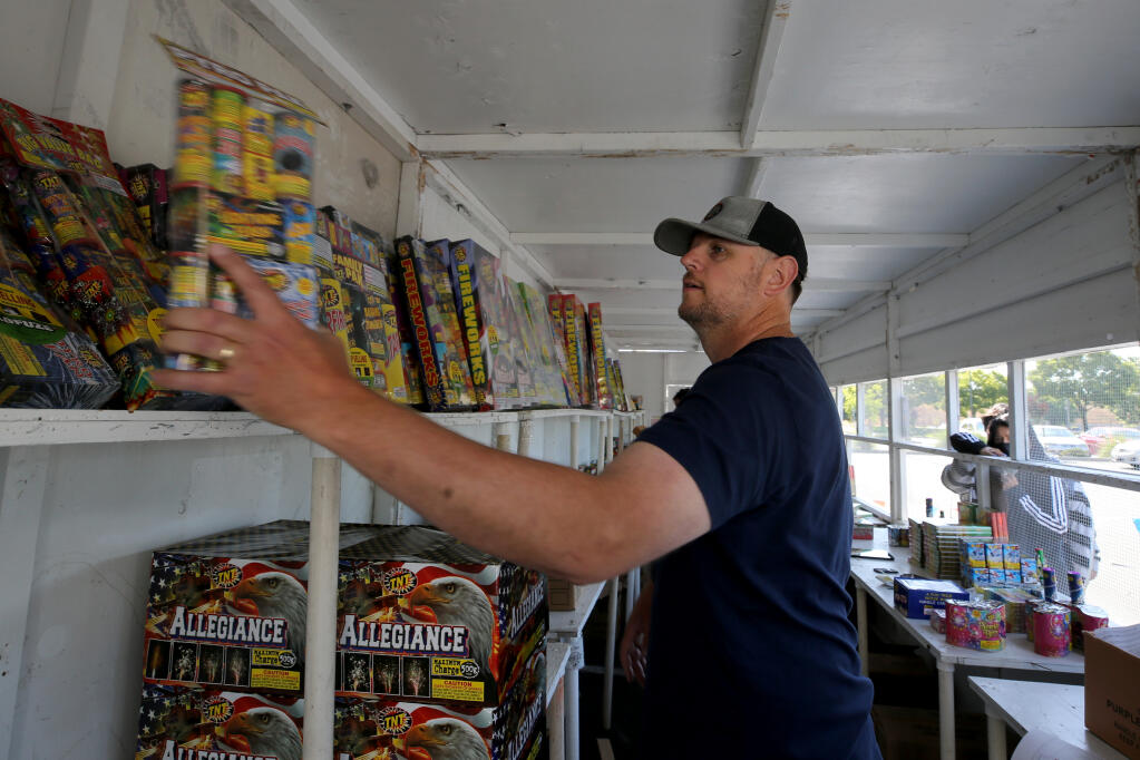 Sean Sage grabs a package of fireworks for a customer at the stand in the Home Depot parking lot in Rohnert Park, Calif., on Wednesday, June 30, 2021.(Beth Schlanker/The Press Democrat)