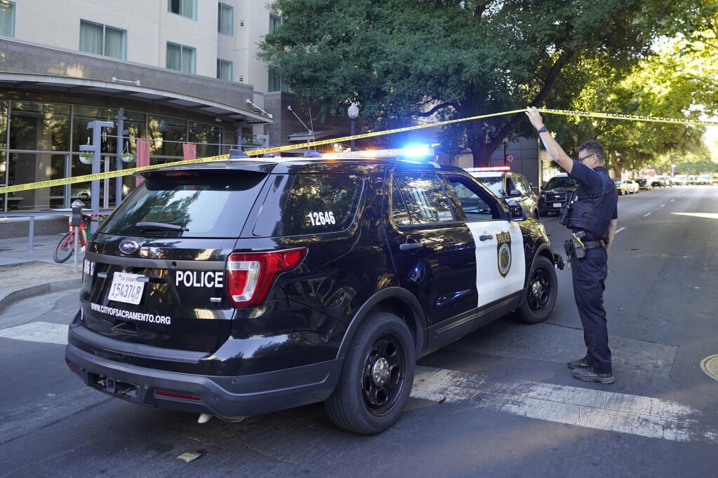 Sacramento Police officer raises police barricade tape as a police vehicle drives to the scene of a fatal shooting that also injured others outside of a downtown Sacramento, Calif., night club in the early morning hours on Monday, July 4, 2022. (AP Photo/Rich Pedroncelli)