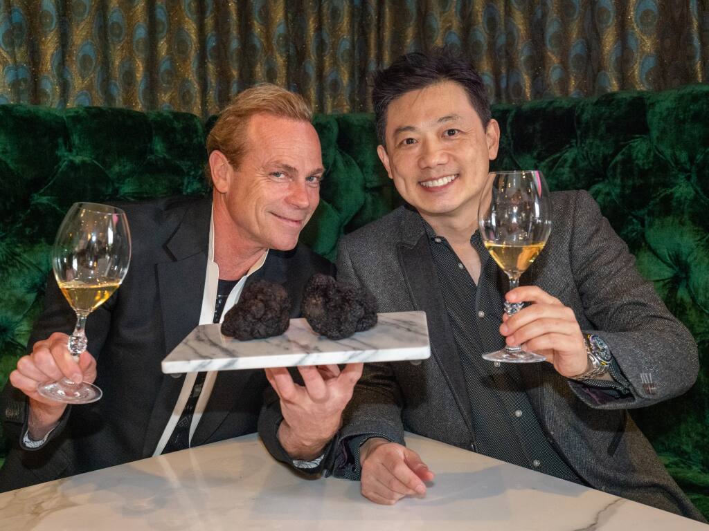 Jean-Charles Boisset of Boisset Collection and Robert Chang of American Truffle Company lift filled wine glasses, while Boisset holds a marble square plate with two Perigord black truffles on it. (courtesy of Boisset Collection)