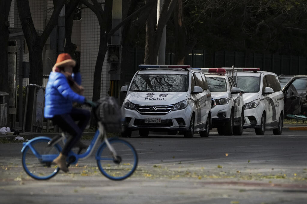 A woman rides past police vehicles parked along a road monitoring near the site of last weekend protest in Beijing, Tuesday, Nov. 29, 2022. With police out in force, there was no word of protests Tuesday in Beijing, Shanghai or other major cities. (AP Photo/Andy Wong)