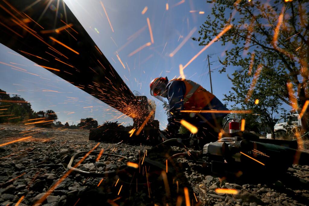 Isiah Romero, an employee of Holland LP, grinds a piece of rail after it was welded as part of a 3-mile extension of the SMART line in Windsor on Tuesday, July 14, 2020. (Beth Schlanker / The Press Democrat)