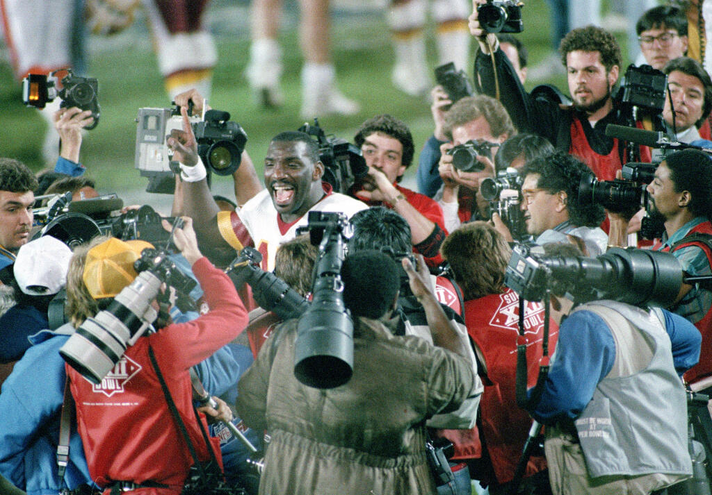 FILE - In this Feb. 1, 1988, file photo, Washington Redskins quarterback Doug Williams is surrounded by members of the media after he led the Redskins to a 42-10 victory over the Denver Broncos in Super Bowl XXII in San Diego, Ca. The history of Super Bowl Media Day, and mandatory player availability, has played a key role in making the Super Bowl most-watched NFL TV program. (AP Photo/File)