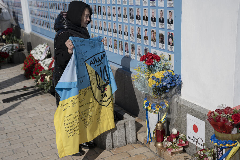 A woman holds a Ukrainian flag next to the Memory Wall of Fallen Defenders of Ukraine in Russian-Ukrainian War on Ukrainian Volunteer Day in Kyiv, Ukraine, Tuesday, March 14, 2023. (AP Photo/Andrew Kravchenko)