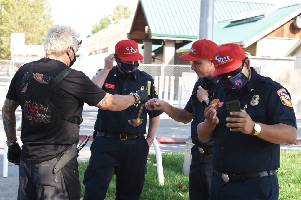 Celebrity restaurateur Guy Fieri, left, offering up meatball samples to firefighters before serving pasta and meatball lunches to some 1,000 firefighters at the Sonoma County Fairgrounds in Santa Rosa, Calif. on Saturday, Oct. 3, 2020. (Erik Castro/For The Press Democrat)