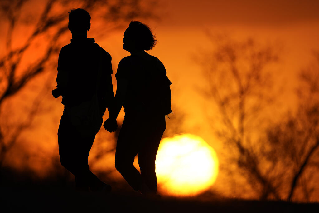 FILE - In this Wednesday, March 10, 2021 file photo, a couple walks through a park at sunset in Kansas City, Mo. According to a report released by the Centers for Disease Control and Prevention on Tuesday, July 20, 2021, U.S. life expectancy fell by a year and a half in 2020, the largest one-year decline since World War II. Worse, the decrease for both Black Americans and Hispanic Americans was a staggering three years. The decrease is due mainly to the COVID-19 pandemic, which health officials say is responsible for close to 74% of the overall life expectancy decline.  (AP Photo/Charlie Riedel, File)
