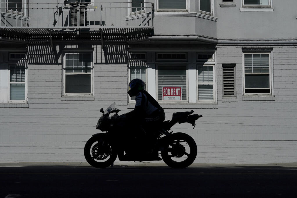 A motorcyclist rides in front of a For Rent sign in a window of a residential property in San Francisco, Tuesday, Oct. 20, 2020. (AP Photo/Jeff Chiu)
