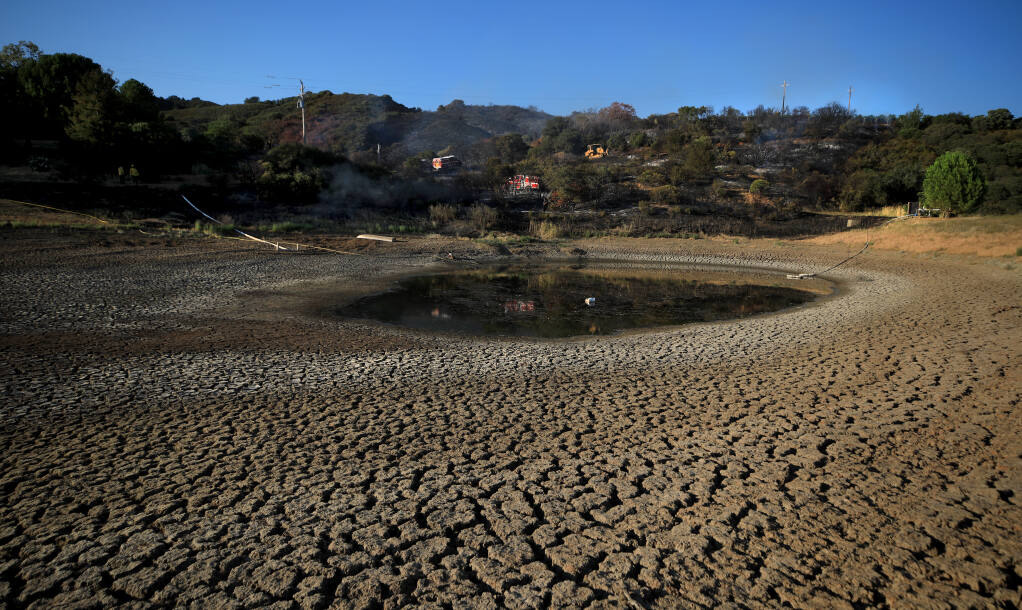 A vineyard pond nearly depleted from several years of drought, serves as a foreground to the Pine Fire in Cloverdale, Tuesday, July 26, 2022. (Kent Porter / The Press Democrat) 2022