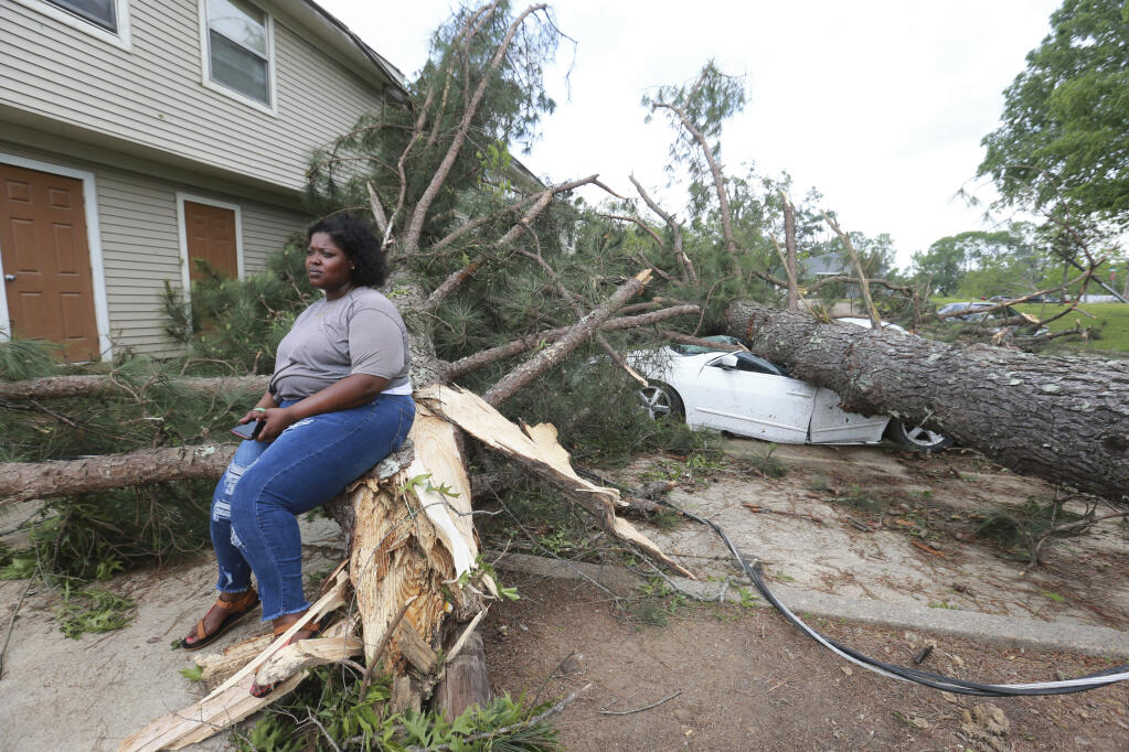 Myesha Gore of Calhoun City, Mississippi sits on the trunk of a shattered pine tree as the rest of tree crushed her car behind her while she was visiting her mother in Vardaman during Sunday's severe weather.(Thomas Wells/Northeast Mississipppi DAily Journal, Via AP))