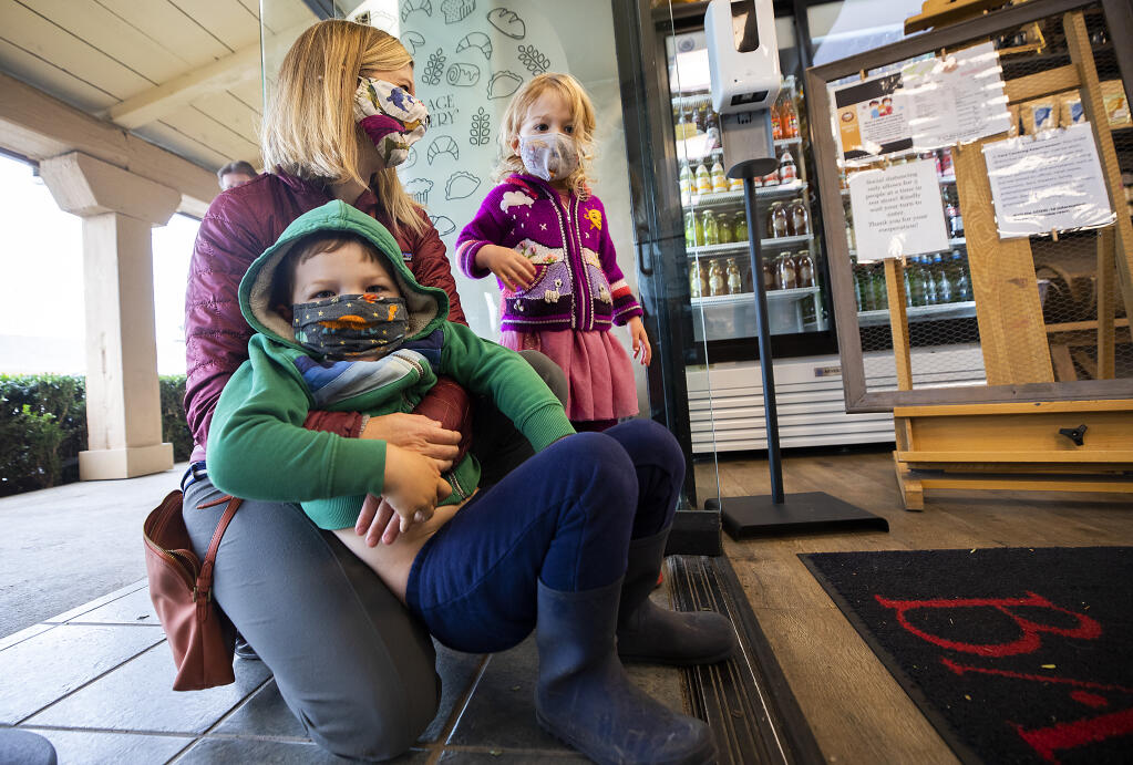 From left, Megan, Reid, 4, and Serena Wilson , 3, wait in line for a special treat at the Village Bakery in Montgomery Village on Friday, November 19, 2021. (Photo by John Burgess/The Press Democrat)