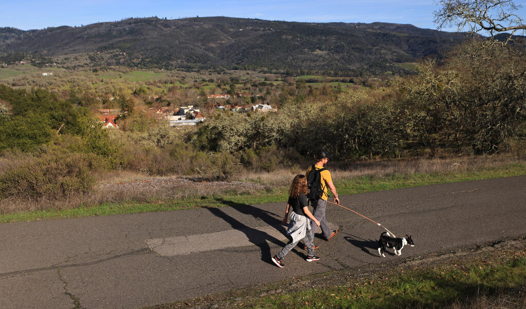 Joe and Owen Uhr of Glen Ellen take their dog Frida for a walk on the upper property of the Sonoma Developmental Center, in Glen Ellen, Thursday, Jan. 4, 2024. The main campus is visible, middle, with a view of the southern Mayacamas Mountains in the background.  650 acres of SDC open space land will now come under the stewardship of California  State Parks. (Kent Porter / The Press Democrat)