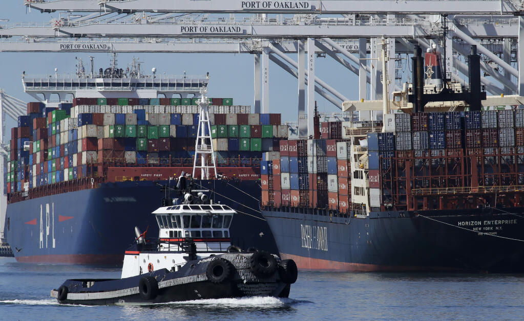 A tugboat passes container ships being unloaded at the Port of Oakland on Wednesday, March 4, 2020, in Oakland, Calif. (AP Photo/Ben Margot)