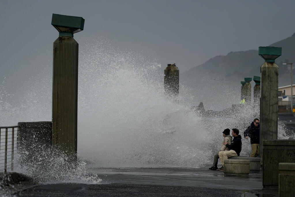People watch as waves crash into a seawall in Pacifica, Calif., Friday, Jan. 6, 2023. California weather calmed Friday but the lull was expected to be brief as more Pacific storms lined up to blast into the state, where successive powerful weather systems have knocked out power to thousands, battered the coastline, flooded streets, toppled trees and caused at least six deaths. (AP Photo/Jeff Chiu)