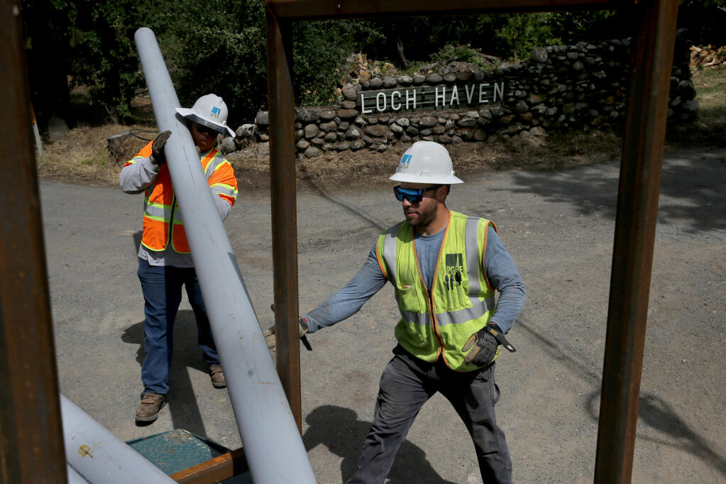 PG&E employees Malik Johnson, left, and Anthony Postlethwait unload conduit tubes used to bury power lines at the intersection of Porter Creek Road  and Loch Haven Drive in Santa Rosa, Calif. on Tuesday, June 7, 2022. (Beth Schlanker/The Press Democrat)