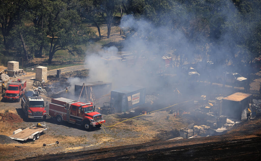 Firefighters tamp out areas around shipping containers that burned during a grass fire Saturday, June 11, 2022, off Riebli Road in Rincon Valley. (Kent Porter / The Press Democrat) 2022