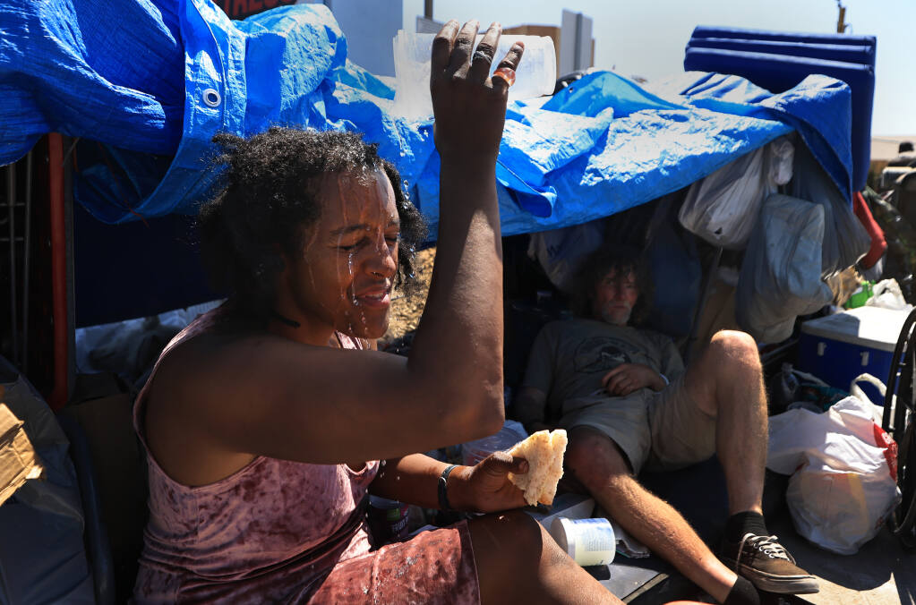 Amid 110 degree heat, Angel Martinez uses her remaining water to cool off at her encampment with Jerry Fullington along Santa Rosa Ave., Monday, Sept. 5, 2022 in Santa Rosa. (Kent Porter / The Press Democrat) 2022