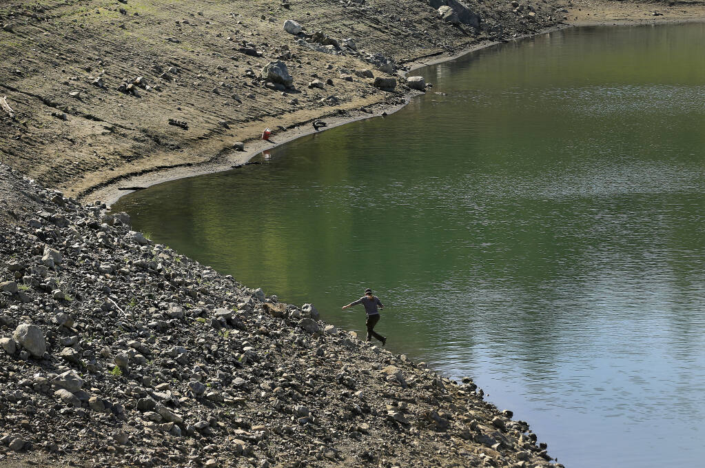A fisherman tries his luck along the receding shoreline at Lake Sonoma, where the impacts of a dry winter are increasingly apparent. (KENT PORTER / The Press Democrat)