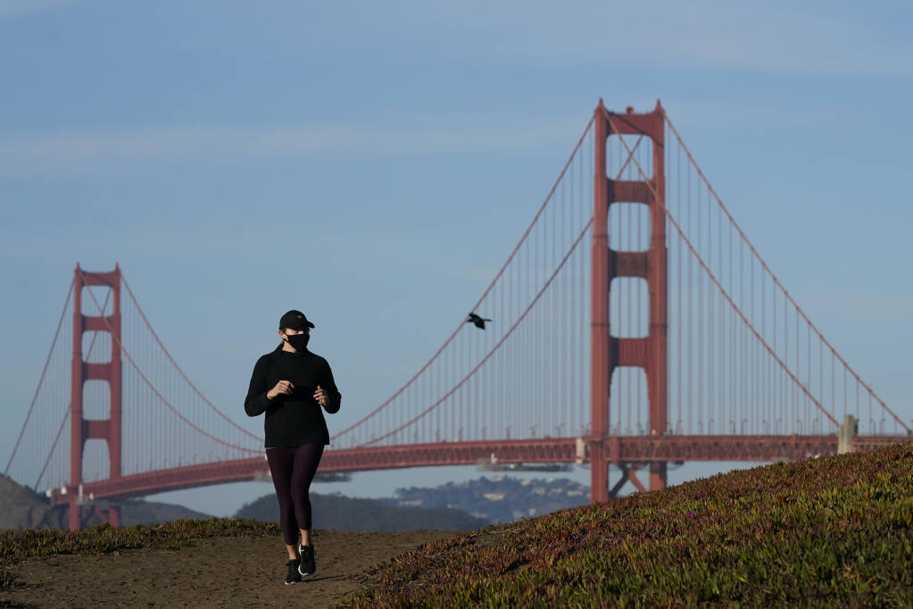 A person wearing a mask runs on a path in front of the Golden Gate Bridge during the coronavirus pandemic in San Francisco, Monday, Nov. 30, 2020. (AP Photo/Jeff Chiu)