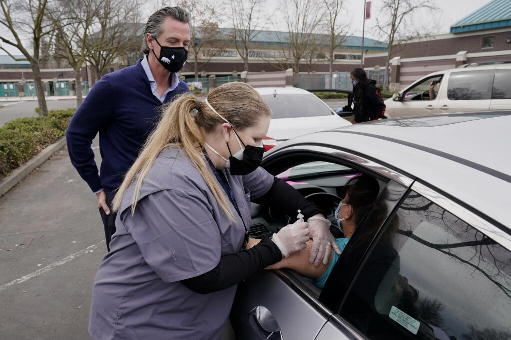 Gov. Gavin Newsom watches as LVN Cari Elkins gives a COVID-19 vaccination at a drive-thru vaccination center at Natomas High School in Sacramento, Calif., Thursday, Feb. 11, 2021. Appointments were needed for the 1,000 vaccinations to be administered for those 65 and over, first responders, health workers, teachers, food and agricultural employers. Called an equitable distribution site, it prioritized those disproportionally impacted by COVID-19, was collaboration between the Natomas' Unified School District, Sacramento County Public Health Department and Sacramento Vice Mayor Angelique Ashby who represents the area. (AP Photo/Rich Pedroncelli)