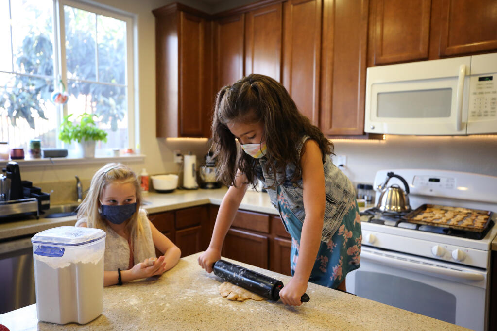 Priya Leach, 7, stands on a chair as she rolls out the dough to make homemade dog treats that she and her friend, Emmie Lenz, 8, are baking and selling as a fundraiser for North Bay Animal Services. Photo taken at the Leach home in Petaluma on Wednesday, March 3, 2021. (Beth Schlanker / The Press Democrat)