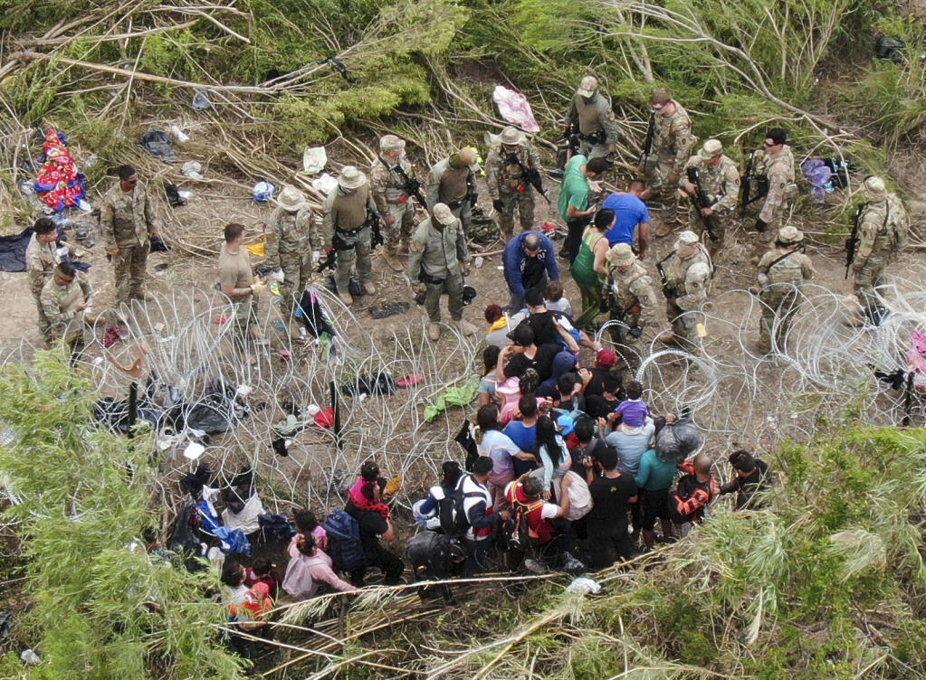 Migrants pass through razor wire on the bank of the Rio Grande river where Texas National Guards verbally tell them not to cross, as migrants enter the U.S. to turn themselves into immigration authorities, seen from Matamoros, Mexico, Thursday, May 11, 2023. Pandemic-related U.S. asylum restrictions, known as Title 42, are to expire May 11. (AP Photo/Fernando Llano)