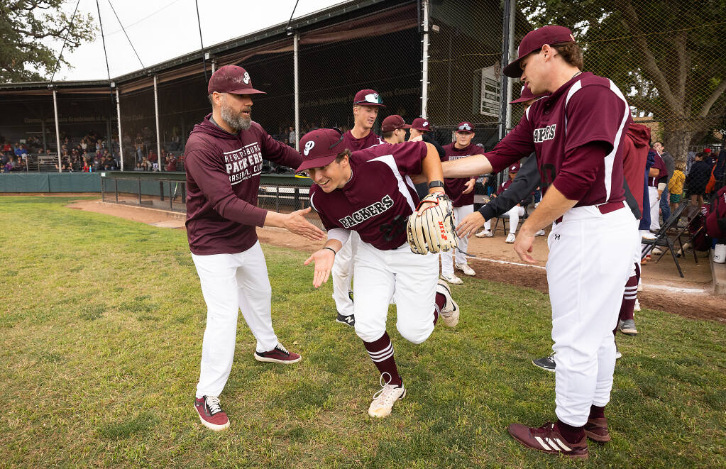 Connor Charpiot sprints out the field past manager Joey Gomes, left, and the Healdsburg Prune Packers on opening day of the California Collegiate League season, June 6, 2023. (Photo by John Burgess / The Press Democrat)