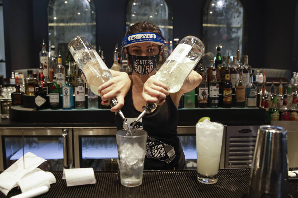 FILE - In this July 1, 2020, file photo, a bartender mixes a drink while wearing a mask and face shield at Slater's 50/50 in Santa Clarita, Calif.  (AP Photo/Marcio Jose Sanchez, File)
