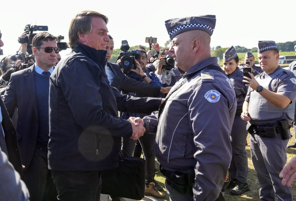 Brazilian President Jair Bolsonaro greets police as he arrives to a resort hotel where he is expected to meet with Elon Musk in Porto Feliz, Brazil, Friday, May 20, 2022. Musk, the Telsa and SpaceX chief executive officer, tweeted that he was in Brazil to help bring Internet service to rural schools in the Amazon and to help monitor the Amazon environmentally. (AP Photo/Andre Penner)