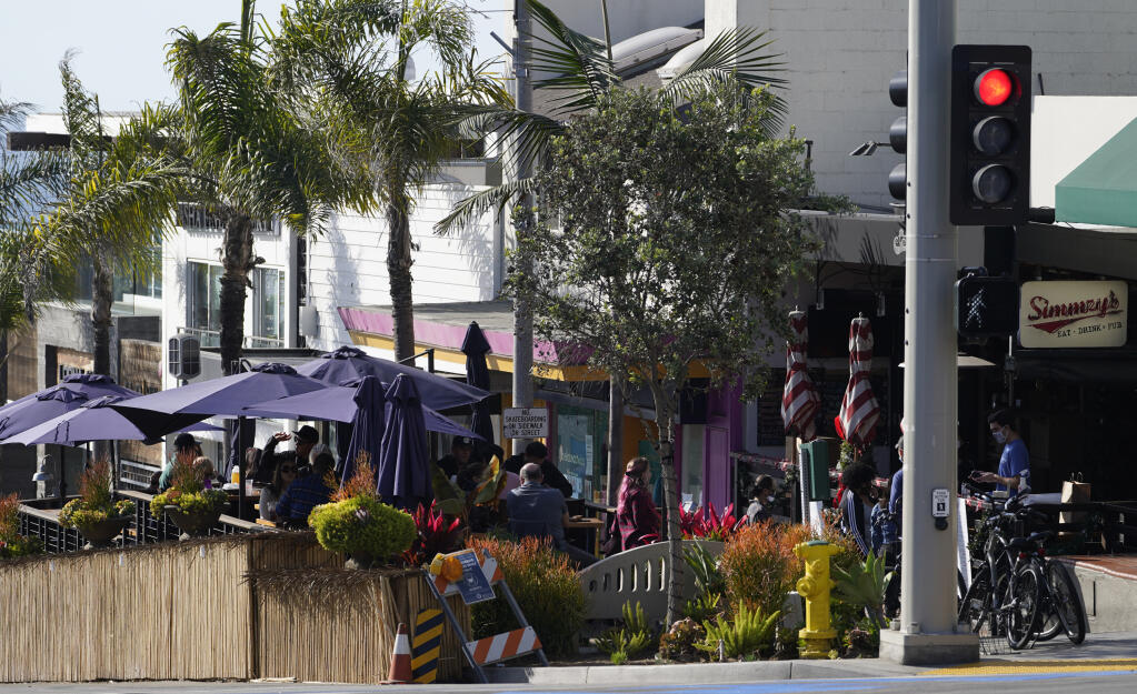Patrons pick up their food to go orders at Simmzy's restaurant counter, right, before sitting to consume their meals at a "Public Parklet" outdoors area, seen left, in Manhattan Beach, Calif., Thursday, Dec. 10, 2020. (AP Photo/Damian Dovarganes)