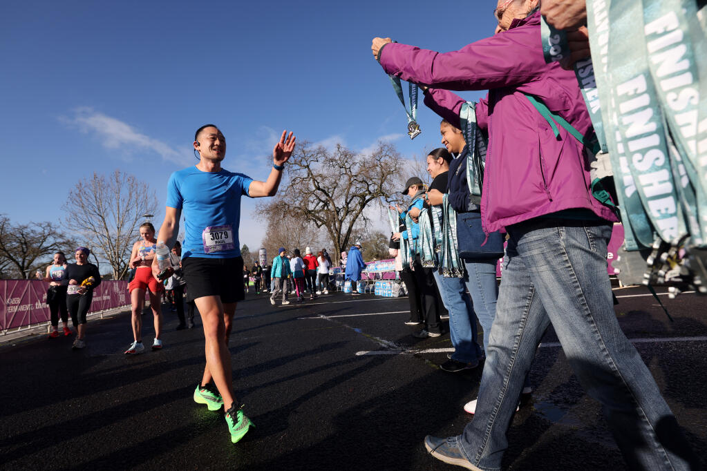 Napa Valley Half-Marathon runner Paul Chung reaches for a participation medal after finishing at Vintage High School in Napa , Sunday, March 3, 2024. (Beth Schlanker/ The Press Democrat)