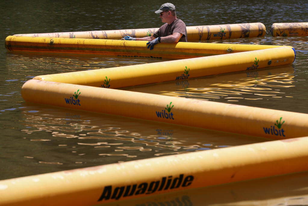 Sonoma County Regional Parks lifeguard James Brooks cleans inflatable barriers while helping to set up the floating water park in the swimming lagoon at Spring Lake Regional Park in Santa Rosa on Tuesday, May 24, 2022.  The swimming lagoon opens on Saturday and will operate through Labor Day.  (Christopher Chung/ The Press Democrat)