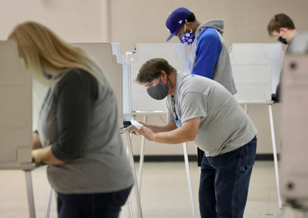 Election Clerk Steve Aja sanitizes a voting booth between voters at the Roseland Community Center in Santa Rosa on Tuesday, Nov. 3, 2020. (Beth Schlanker / The Press Democrat)