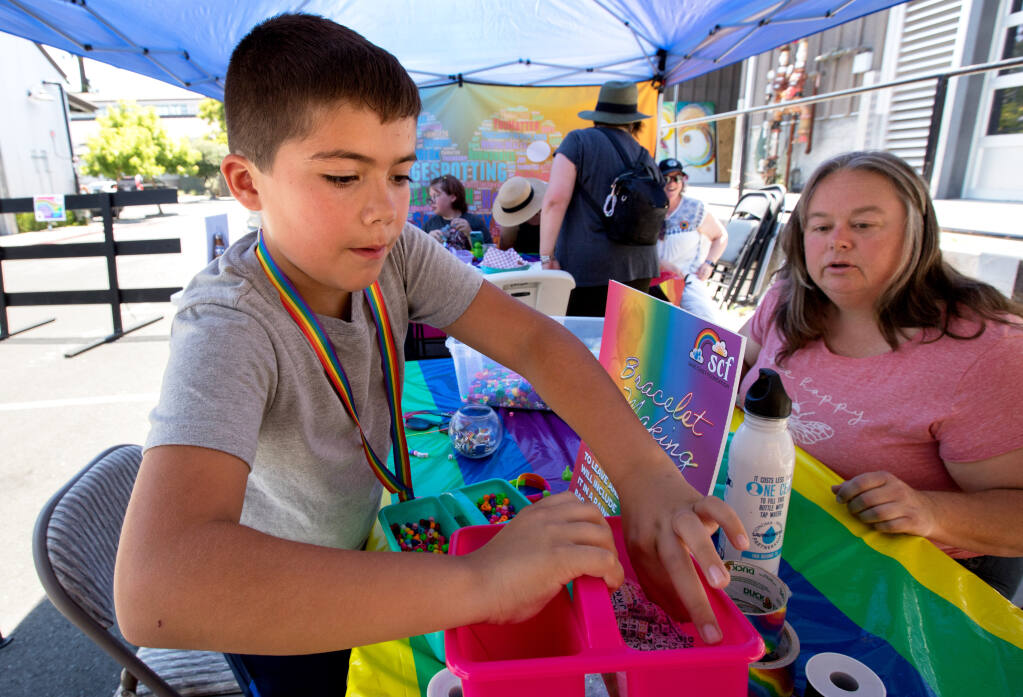 Luca Hartigan, 10, of Santa Rosa, picks out beads to make a bracelet with volunteer Judy Teixeira, of Santa Rosa, helping, as children enjoy arts and crafts at the Rainbow Party benefit for the Sage Casey Foundation at Crooked Goat Brewing in Sebastopol, Saturday, July 22, 2023. (Darryl Bush / For The Press Democrat)
