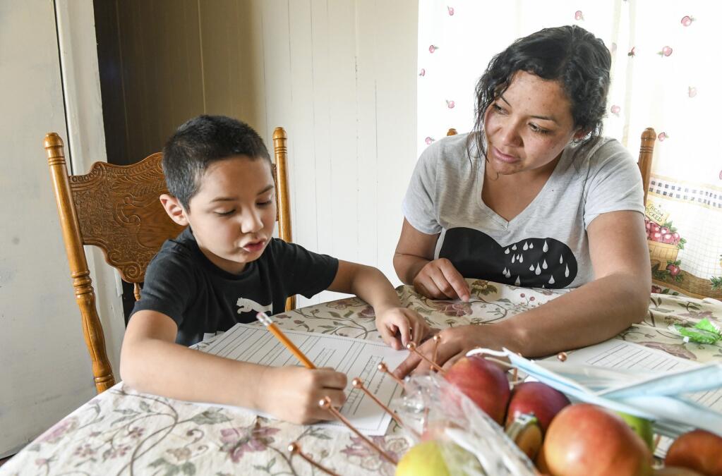 Carolina Navarro, 34, helps her son Cesar Alejandro with his homework at their mobile home in Cantua Creek on Tuesday, March 2, 2021. Navarro is divorced with two children and has been out of work since November.