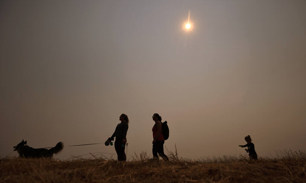 From left, Lucy Whitney, Sarah Jacobs and her daughter, Charlotte, take Finn for a walk at Crane Creek Regional Park near Rohnert Park, as smoke from forest fires in far Northern California settles in, Friday, Aug. 6, 2021. (Kent Porter / The Press Democrat) 2021