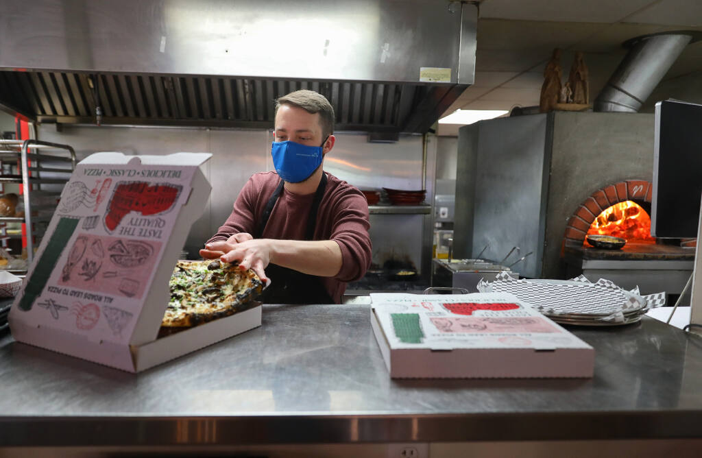 Head cook Hayden Berry slides a pizza into a takeout box at Franchettis' Gasthaus + Kitchen in Santa Rosa on Tuesday, May 4, 2021.  (Christopher Chung/ The Press Democrat)