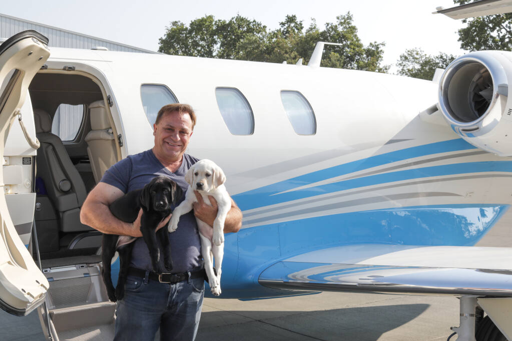 Jordan Vineyard & Winery owner John Jordan poses with two puppies in 2021 before they fly from Sonoma County to the dogs’ volunteer raisers, in partnership with Santa Rosa-based Canine Companions. (Jordan Vineyard & Winery)