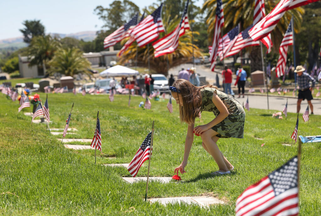 Sophia Norona, 9, places flowers on graves of military veterans following the Memorial Day ceremony at Cypress Hill Memorial Park in Petaluma, Monday, May 30, 2022. (Christopher Chung / The Press Democrat file)