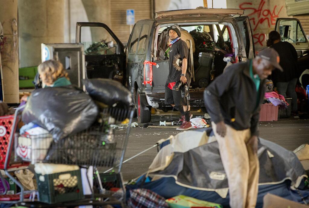 A homeless person prepares to move on from their camp in a parking lot under Highway 101 near 4th Street after Santa Rosa Police on Wednesday morning ordered all in the encampment to move on by Thursday.   ( John Burgess/The Press Democrat).