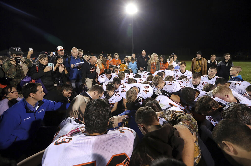 Coach Joseph Kennedy is surrounded by players as they kneel and pray with him on the field after an Oct. 16, 2015 game in Bremerton, Washington. (MEEGAN M. REID / Kitsap Sun)