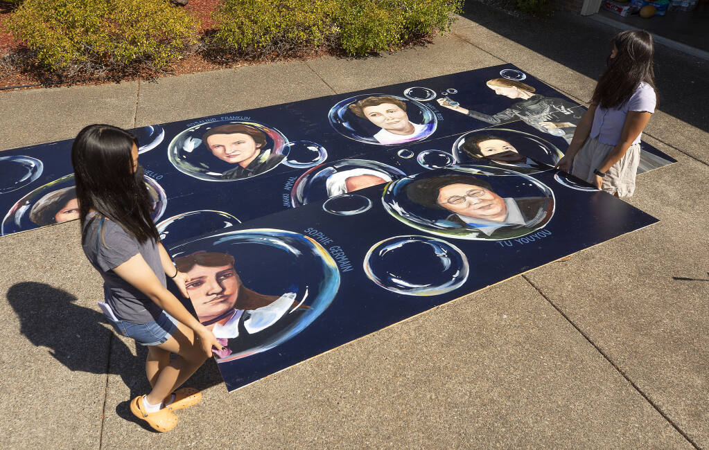 Emma Chen, right, and Teresa Liang carry one panel of their 32-by-8 mural of 10 female STEM historical leaders back into Emma's garage for storage before it is installed next month outside the Petaluma library.  (John Burgess/The Press Democrat)