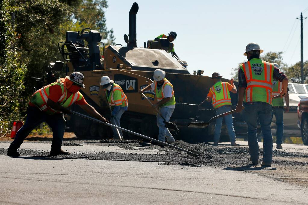 Workers with Ghilotti Bros. Contractors spread asphalt as they repave Barnett Valley Road at Bodega Highway outside Sebastopol on Wednesday, July 29, 2020. (Alvin Jornada / The Press Democrat)